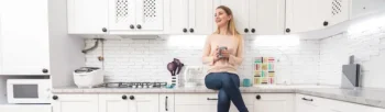 Woman smiling and sitting on kitchen counter with coffee - Inspect-All Services Pest Control in Atlanta, GA