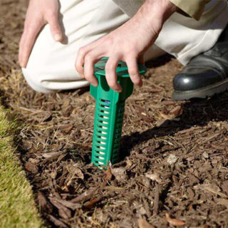 Pest control technician placing a green termite bait station in a garden bed